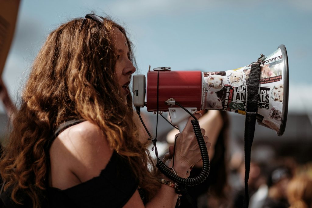 A woman speaking passionately into a megaphone adorned with advocacy stickers, symbolizing empowerment and the courage to speak up.