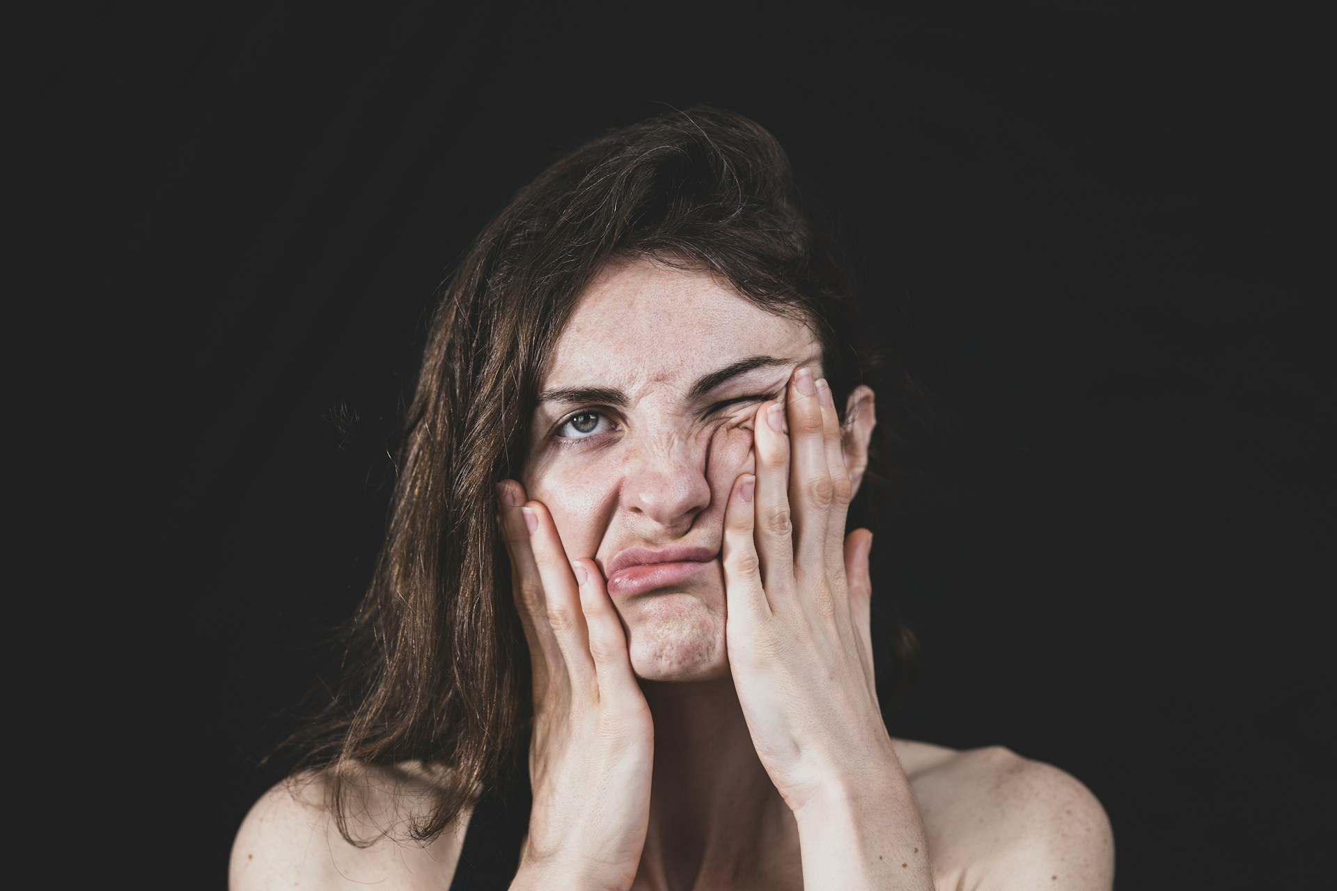 A woman pressing her hands against her face with a frustrated expression, symbolizing emotional struggles and inner tension.
