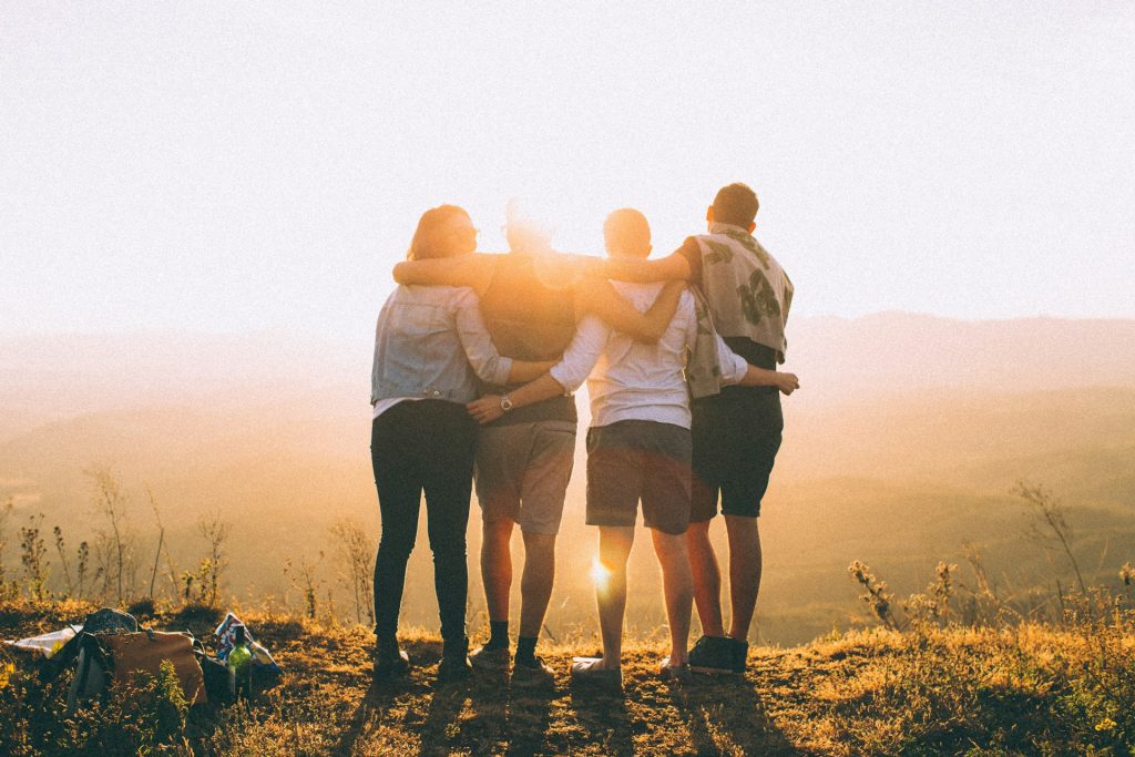 Four friends embracing as they watch the sunrise, symbolizing unity and shared experiences.