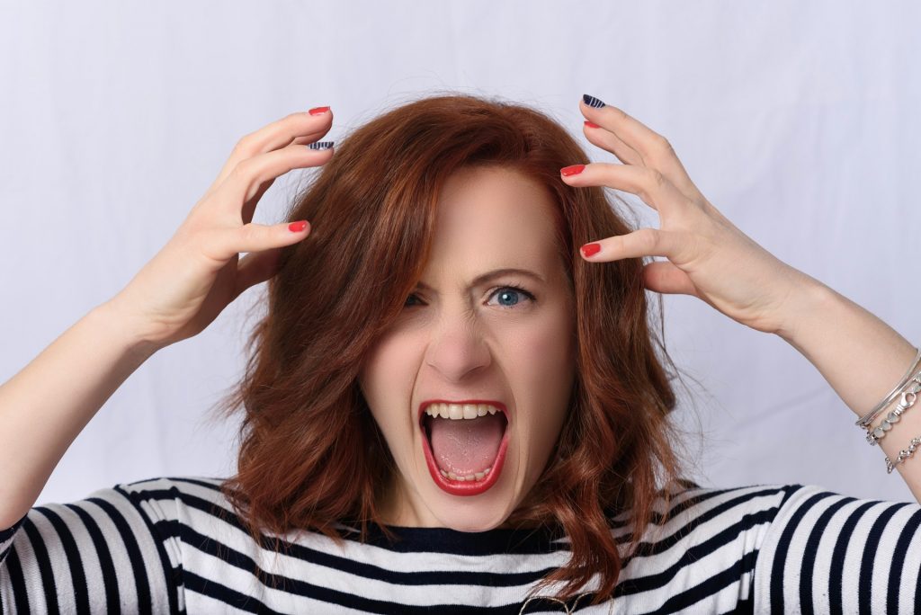 A frustrated woman with red hair screaming and holding her head in exasperation, symbolizing stress, emotional tension, and anxiety.