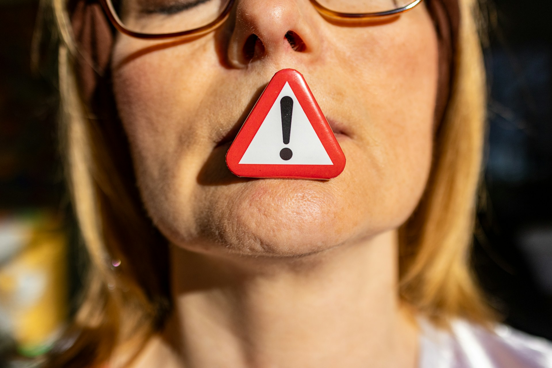 A close-up of a woman's face with a triangular warning sign covering her lips, symbolizing silence, caution, and suppressed communication.