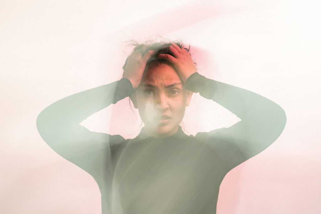 A distressed woman with her hands on her head, her expression conveying anxiety and confusion, surrounded by a blurred, ethereal glow.