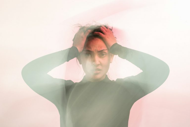 A distressed woman with her hands on her head, her expression conveying anxiety and confusion, surrounded by a blurred, ethereal glow.